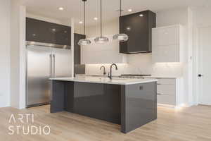 Kitchen featuring a kitchen island with sink, white cabinets, light hardwood / wood-style floors, hanging light fixtures, and built in fridge