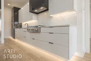 Kitchen with decorative backsplash, light hardwood / wood-style flooring, wall chimney range hood, and stainless steel gas cooktop