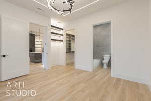 Unfurnished bedroom featuring a walk in closet, tile walls, connected bathroom, light hardwood / wood-style floors, and a chandelier