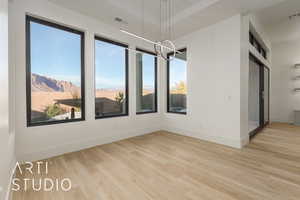 Spare room featuring an inviting chandelier, a healthy amount of sunlight, and light hardwood / wood-style floors