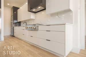 Kitchen featuring stainless steel gas stovetop, white cabinets, wall chimney range hood, tasteful backsplash, and light hardwood / wood-style floors