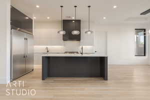 Kitchen featuring a kitchen island with sink, built in fridge, white cabinets, light wood-type flooring, and decorative light fixtures