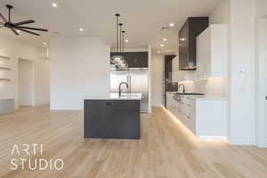 Kitchen with white cabinets, an island with sink, decorative light fixtures, and light wood-type flooring