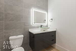 Bathroom with vanity, toilet, wood-type flooring, and tile walls