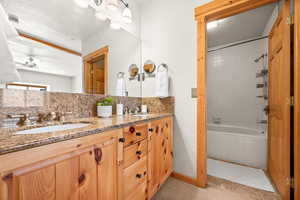 Bathroom featuring vanity, tasteful backsplash, tiled shower / bath combo, and ceiling fan