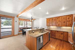 Kitchen with a center island with sink, sink, stainless steel dishwasher, light wood-type flooring, and beamed ceiling