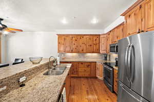 Kitchen with light stone countertops, appliances with stainless steel finishes, ceiling fan, sink, and light hardwood / wood-style floors