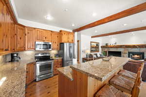 Kitchen featuring appliances with stainless steel finishes, a kitchen island, beam ceiling, light hardwood / wood-style floors, and a stone fireplace