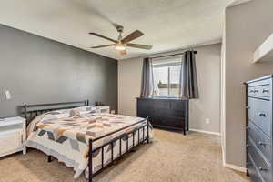 Bedroom with ceiling fan, light carpet, and a textured ceiling