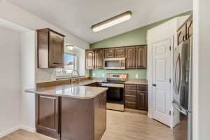 Kitchen featuring dark brown cabinets, stainless steel appliances, vaulted ceiling, sink, and light hardwood / wood-style flooring