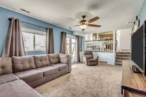 Living room featuring ceiling fan, light colored carpet, and a textured ceiling