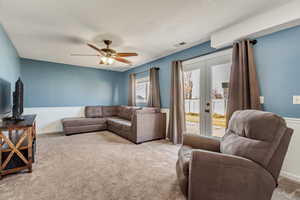 Living room with ceiling fan, light colored carpet, a textured ceiling, and french doors