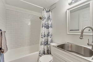 Full bathroom featuring toilet, sink, a textured ceiling, and shower / tub combo with curtain