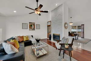 Living room featuring a fireplace, high vaulted ceiling, wood-type flooring, and ceiling fan with notable chandelier