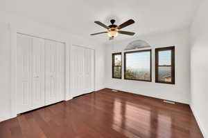 Unfurnished bedroom featuring ceiling fan, dark hardwood / wood-style floors, and multiple closets