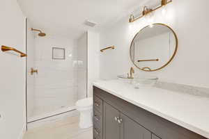 Bathroom with tiled shower, vanity, and toilet