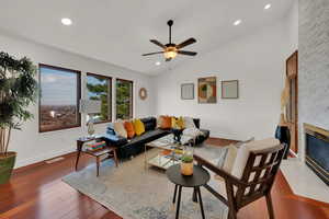 Living room with hardwood / wood-style floors, ceiling fan, lofted ceiling, and a fireplace