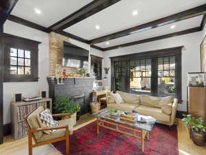 Living room featuring beamed ceiling, ornamental molding, a brick fireplace, and hardwood flooring