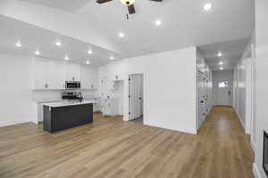 Kitchen with vaulted ceiling, an island with sink, appliances with stainless steel finishes, light hardwood / wood-style floors, and white cabinetry