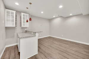 Kitchen featuring kitchen peninsula, light stone counters, a breakfast bar, wood-type flooring, and hanging light fixtures