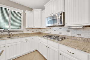 Kitchen with sink, stainless steel appliances, light tile patterned floors, light stone counters, and white cabinets