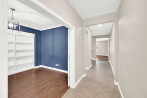 Corridor featuring hardwood / wood-style flooring, built in shelves, ornamental molding, and a chandelier