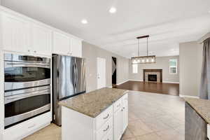 Kitchen with a center island, a tile fireplace, white cabinets, hanging light fixtures, and appliances with stainless steel finishes