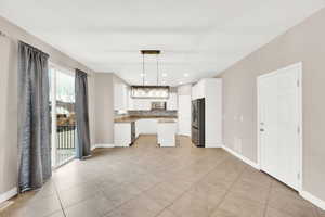 Kitchen with appliances with stainless steel finishes, backsplash, light tile patterned floors, decorative light fixtures, and white cabinetry