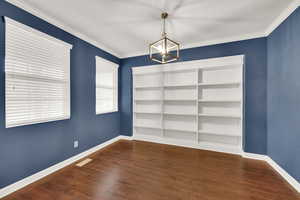 Empty room with a chandelier, dark hardwood / wood-style floors, and ornamental molding