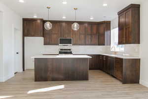 Kitchen featuring stainless steel appliances, sink, decorative light fixtures, a center island, and dark brown cabinetry