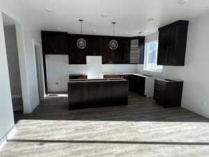 Kitchen featuring hanging light fixtures, a center island, dark wood-type flooring, and dark brown cabinets