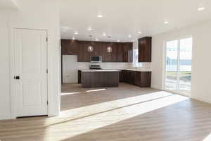 Kitchen with light hardwood / wood-style flooring, dark brown cabinetry, a kitchen island, pendant lighting, and appliances with stainless steel finishes