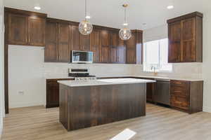 Kitchen featuring pendant lighting, tasteful backsplash, a kitchen island, light wood-type flooring, and appliances with stainless steel finishes