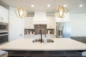 Kitchen with a center island with sink, stainless steel appliances, and custom exhaust hood