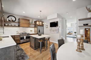 Kitchen with a kitchen bar, appliances with stainless steel finishes, sink, pendant lighting, and light hardwood / wood-style floors