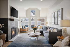 Living room featuring a tiled fireplace, light hardwood / wood-style floors, and lofted ceiling