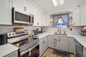 Kitchen with decorative backsplash, stainless steel appliances, sink, pendant lighting, and light hardwood / wood-style floors