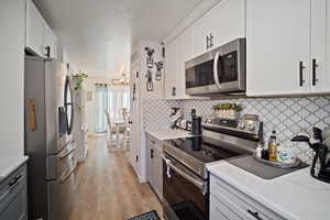 Kitchen featuring white cabinetry, light hardwood / wood-style flooring, stainless steel appliances, and light stone counters