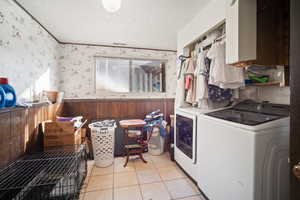 Laundry area featuring light tile patterned floors, separate washer and dryer, and wooden walls