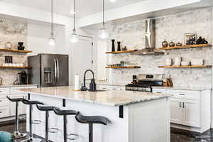 Kitchen featuring light stone countertops, white cabinets, wall chimney range hood, and appliances with stainless steel finishes