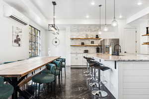 Kitchen featuring backsplash, stainless steel fridge, light stone countertops, decorative light fixtures, and white cabinetry