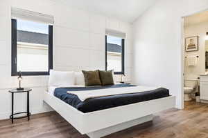 Bedroom featuring hardwood / wood-style floors, vaulted ceiling, connected bathroom, and multiple windows