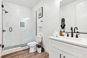 Bathroom with hardwood / wood-style flooring, vanity, toilet, and an enclosed shower