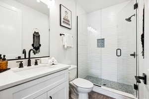 Bathroom with hardwood / wood-style flooring, vanity, toilet, and a shower with door