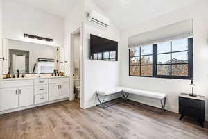 Bathroom featuring vanity, an AC wall unit, hardwood / wood-style floors, toilet, and lofted ceiling