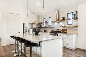 Kitchen featuring white cabinets, wall chimney exhaust hood, stainless steel appliances, and a wealth of natural light