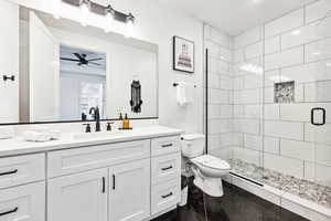 Bathroom featuring vanity, toilet, ceiling fan, and a shower with shower door