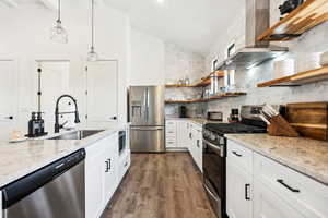 Kitchen with white cabinets, sink, wall chimney exhaust hood, light stone counters, and stainless steel appliances