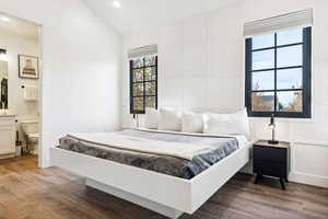 Bedroom with dark wood-type flooring, ensuite bath, and lofted ceiling