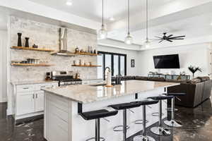 Kitchen featuring stainless steel range with gas cooktop, sink, wall chimney range hood, decorative light fixtures, and white cabinetry